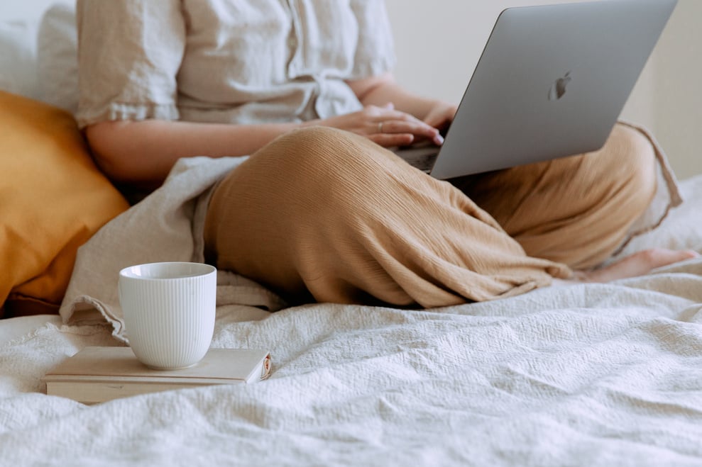 Woman Lounging With Laptop And Cup Of Coffee On The Bed